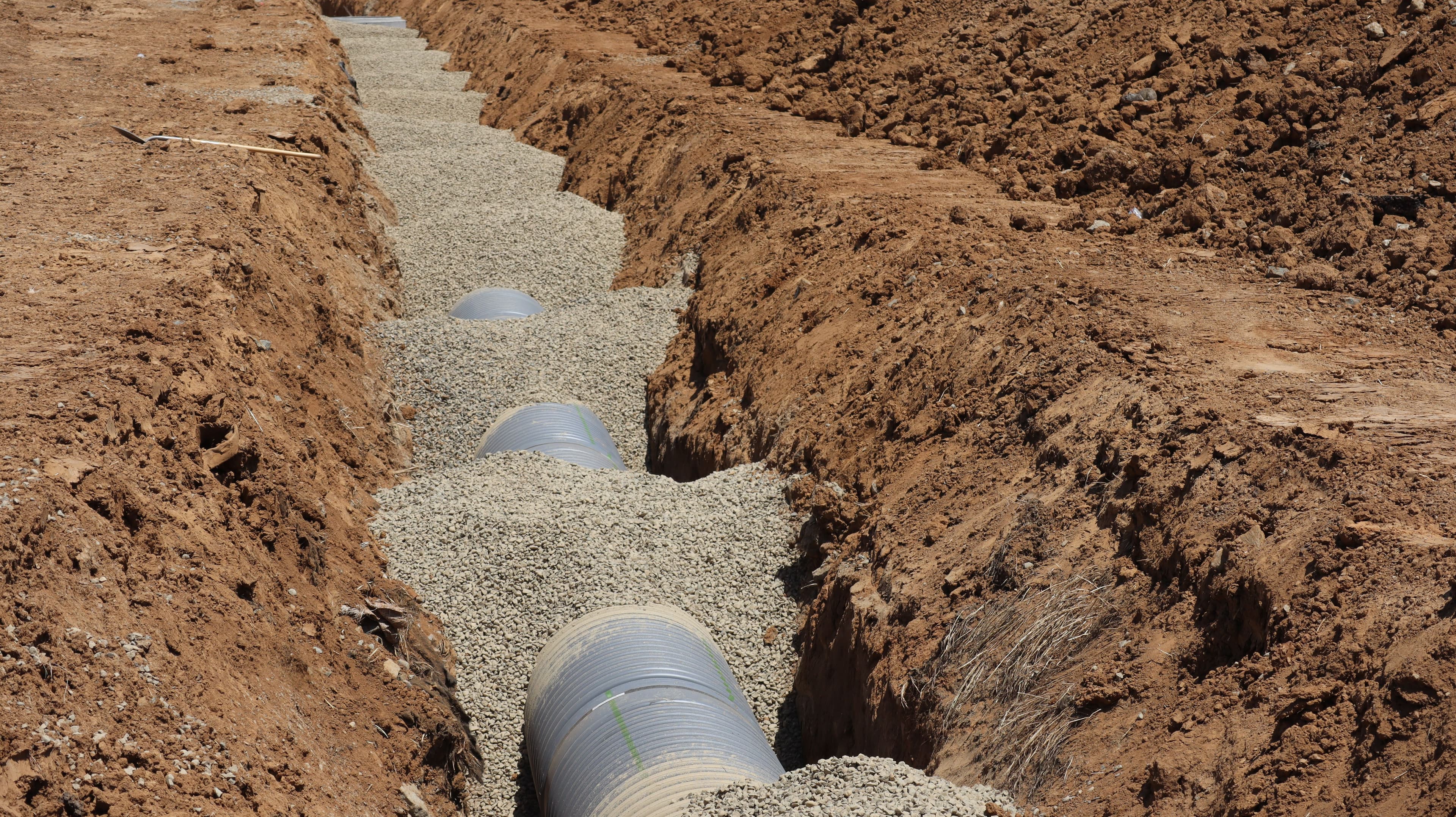 Large corrugated pipes installed in a deep earthen trench and bedded with grey gravel.